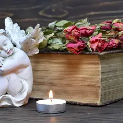 Figurka aniołka, stara księga, świeca i uschnięte róże na drewnianym tle.